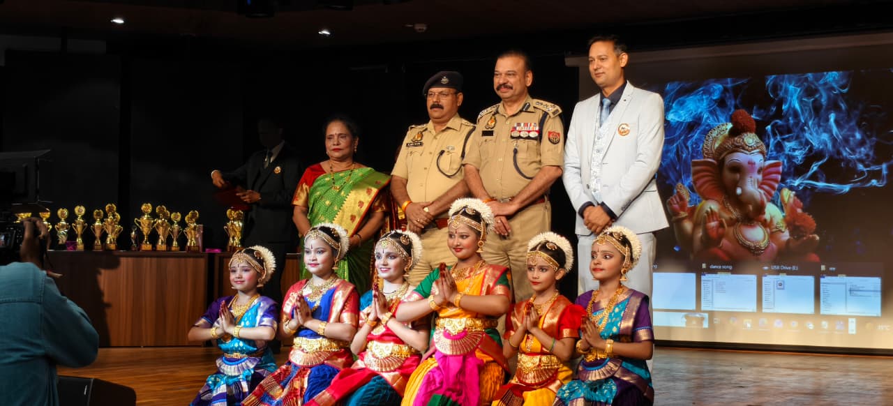 Classical dancers and guests on stage with a Ganesha image on the screen